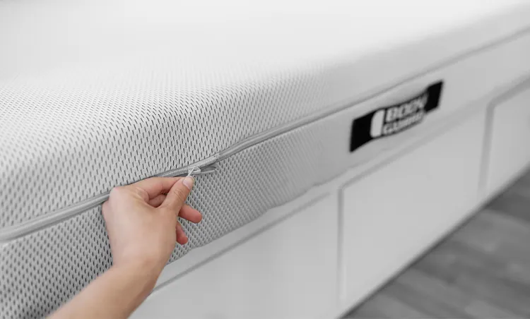 Mano sujetando la cremallera del colchón Bodyguard, detalle de la funda de malla blanca.