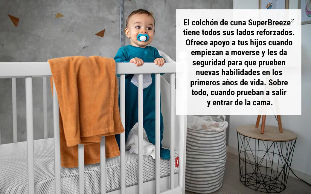 magen de un colchón junto a ropa colgada en una cuna, con un texto que resalta la seguridad de la funda lavable a 60 grados, lo que garantiza un entorno higiénico y seguro para el bebé.