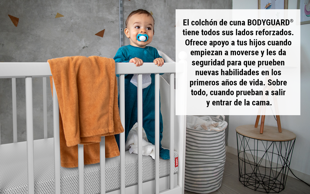 magen de un colchón junto a ropa colgada en una cuna, con un texto que resalta la seguridad de la funda lavable a 60 grados, lo que garantiza un entorno higiénico y seguro para el bebé.