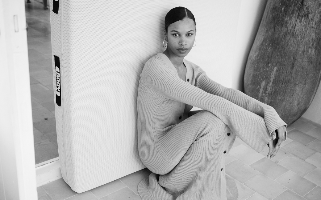 Mujer sentada apoyada sobre un colchón, imagen en blanco y negro.