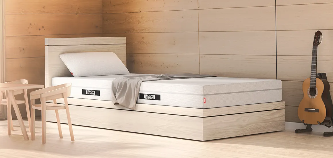 Colchón BODYGUARD® sobre una cama de madera clara en un dormitorio acogedor con guitarra y rincón de comedor.