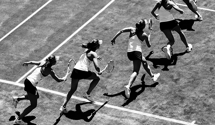 Schwarz-Weiß-Foto von oben: Auf einem Rasen mit Linien ist mehrfach dieselbe Person in unterschiedlichen Bewegungsmomenten beim Rennen mit Tennisschläger zu sehen.