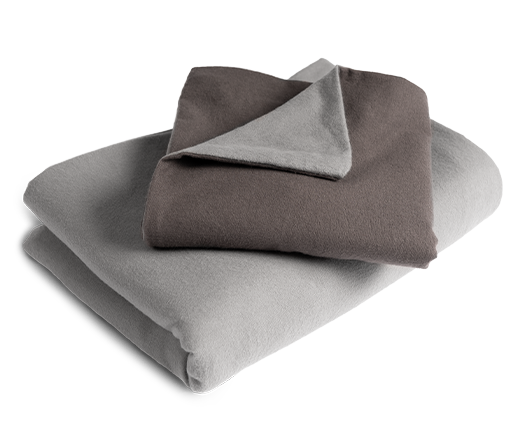 La ropa de cama de franela BODYGUARD® doblada: la funda de edredón está plegada con el lado plateado hacia afuera, y la funda de almohada con el lado color antracita.
