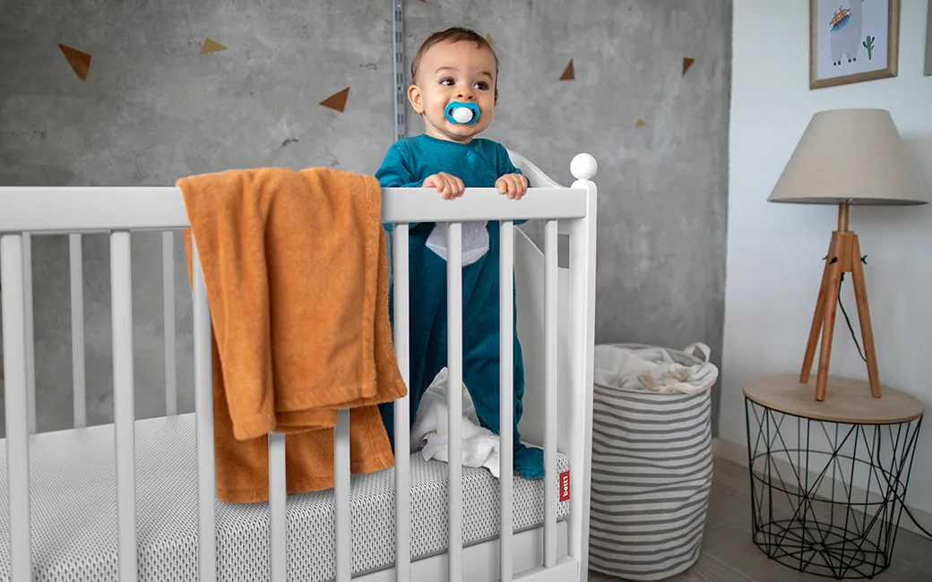 Baby steht in Gitterbett auf der SuperBreeze® Kindermatratze