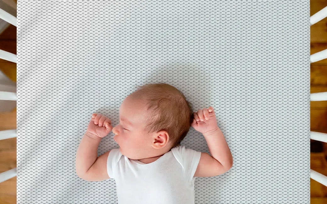 Ein Baby liegt rücklings auf der SuperBreeze Kindermatratze in einem Gitterbett.
