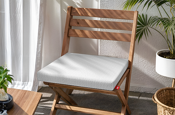Cojín para silla Bodyguard colocado sobre una silla de madera en un entorno doméstico con cortinas y luz natural.