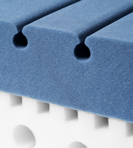 Primer plano del núcleo de espuma bicolor de un colchón, con la parte superior en azul y la inferior en blanco, mostrando las perforaciones que mejoran la ventilación y el soporte