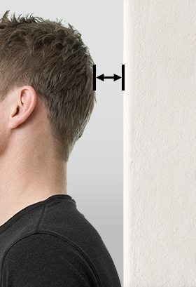 Eine Person steht mit dem Rücken zur Wand, zwischen Wand und Hinterkopf ist ein Pfeil eingezeichnet