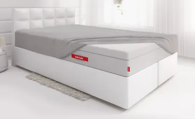 Die FLIP® Matratze ist bis auf eine Ecke mit dem Spannbettlaken extra hoch bezogen und liegt auf einem Boxspringbett in einem hellen Schlafzimmer	